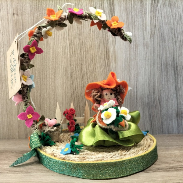 Bambolina con base e arco di fiori con fiori e steccato